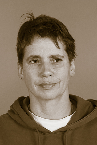 Sepia-Portrait einer Frau. Sie trägt burschikoses, dunkles Haar und ein weißes t-Shirt, darüber ein graues Kapuzenshirt. Ihr Blick geht nach rechts an der Kamera vorbei.